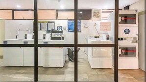 A laundry facility with multiple washing machines and dryers, a wall-mounted control panel, and a QR code for digital access.