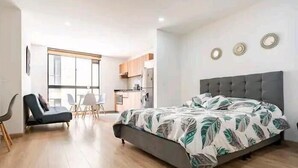 A modern bedroom with a bed, a chair, a dining table, and a kitchen area.