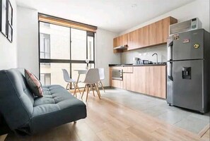 A modern kitchen with wooden cabinets, a stainless steel refrigerator, and a dining area with a white table and chairs. - Hermoso Apartaestudio en centro Bogotá (Bogotá)