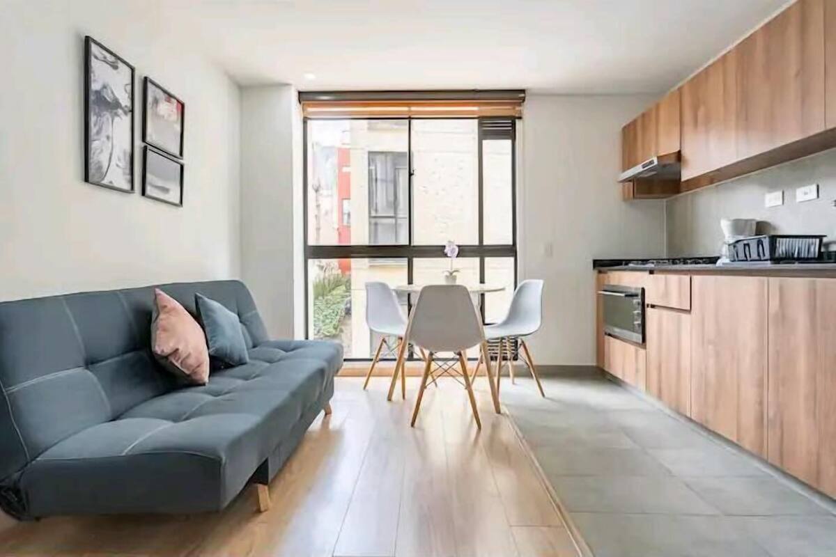 Ein modernes Wohnzimmer mit einem grauen Sofa, einem Esstisch mit Stühlen und einer Küchenzeile mit Holdekor und einer Mikrowelle.