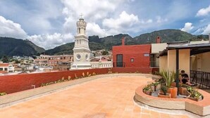 A rooftop terrace with a clock tower, red buildings, and mountainous background.
