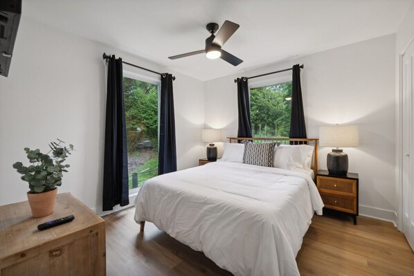 Un dormitorio con una cama, dos mesitas de noche, un ventilador de techo y una ventana con cortinas.