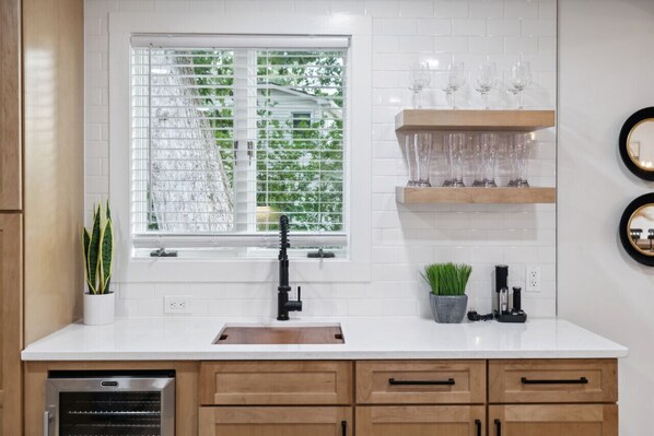 A kitchen with a window, white tiles, wooden cabinets, a sink, and a dishwasher.