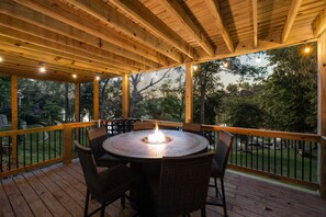 A covered outdoor patio with a round table and chairs, a fire feature, and a view of trees.