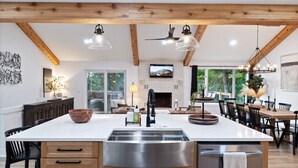 A spacious kitchen with a large island, wooden beams, pendant lights, and a fireplace.