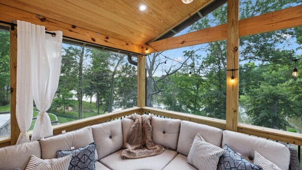 A corner seating area with a cushioned sofa, a draped white curtain, and a view of trees through large windows.