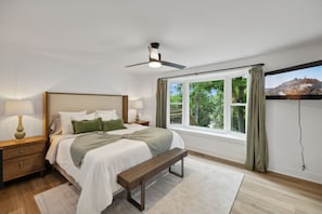 A bedroom with a bed, bedside tables, a bench, a ceiling fan, and a window with curtains.