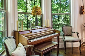 A grand piano in a room with large windows, a vase with yellow flowers, and two chairs.