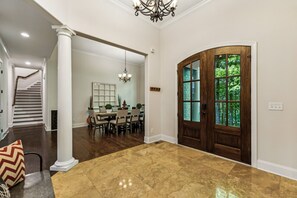 A spacious foyer with a polished marble floor, a grand wooden door with glass panels, and a chandelier.