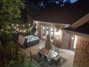 A backyard with a hot tub, a table with chairs, and string lights.