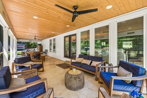 A covered outdoor seating area with sofas and chairs, large windows, and a ceiling fan. - Urban Rustic Lakeside Retreat with Dock, Sleeps 20 (Gallatin)