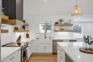 A modern kitchen with white cabinetry, wooden shelves, a large island, and a hanging pendant light.