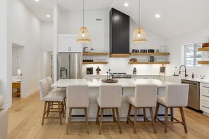 A modern kitchen with a central island, wooden chairs, pendant lights, and built-in shelving. - Urban Rustic Lakeside Retreat with Dock, Sleeps 20 (Gallatin)