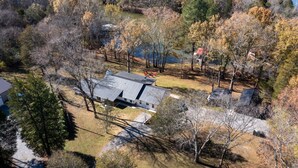A house with a sloped roof, surrounded by trees and a body of water. - Urban Rustic Lakeside Retreat with Dock, Sleeps 20 (Gallatin)