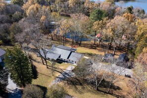 A house with a sloped roof, surrounded by trees and a body of water. - Urban Rustic Lakeside Retreat with Dock, Sleeps 20 (Gallatin)