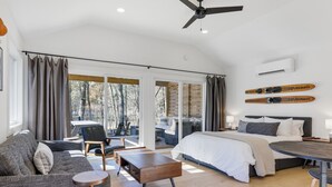 A modern bedroom with a large bed, a sofa, a coffee table, and a ceiling fan. There are skis on the wall and a sliding glass door leading to a balcony. - Urban Rustic Boathouse on Cove (Gallatin)