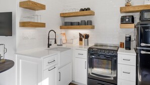 A modern kitchen with white cabinets, wooden shelves, a stainless steel stove, and a black refrigerator. - Urban Rustic Boathouse on Cove (Gallatin)