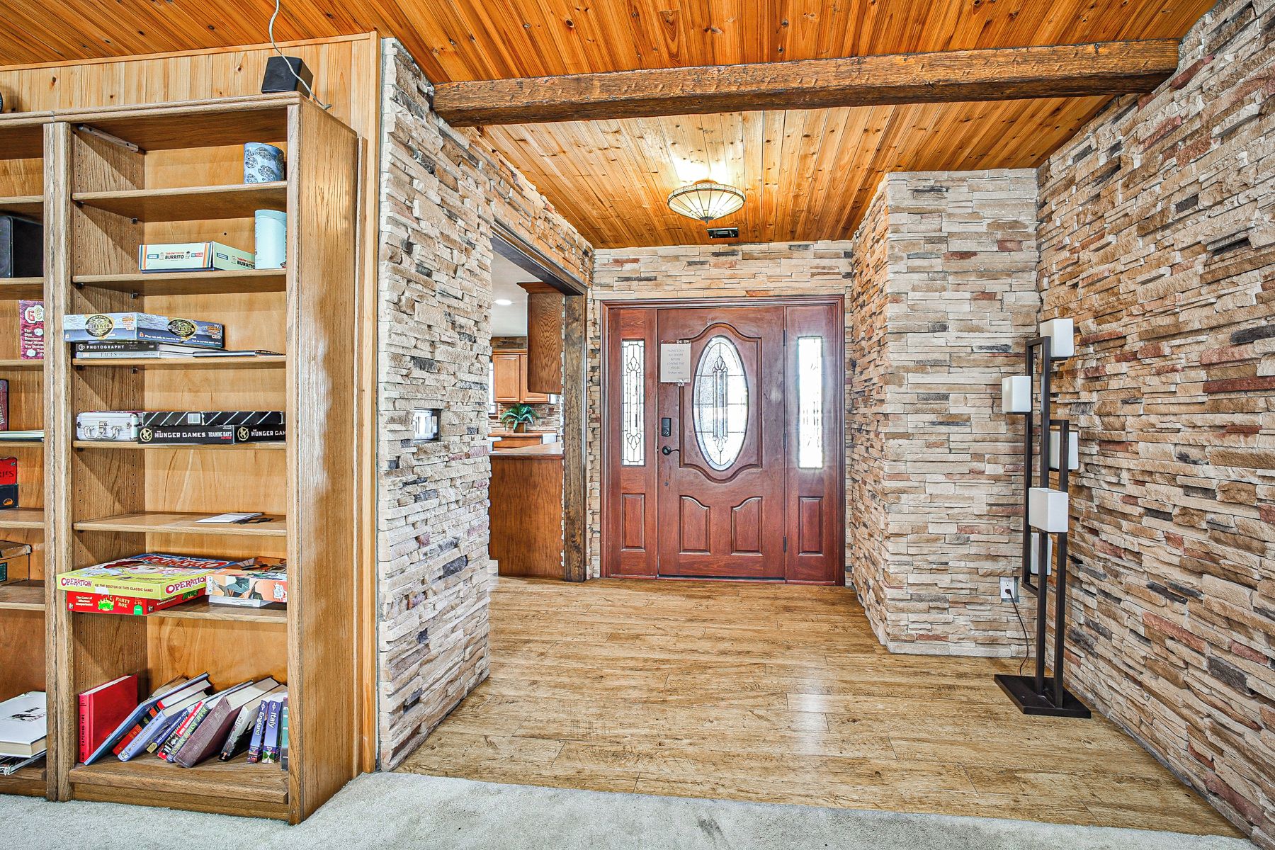 Un pasillo con una estantería de madera, una pared de piedra y una puerta de madera con un panel de vidrio.