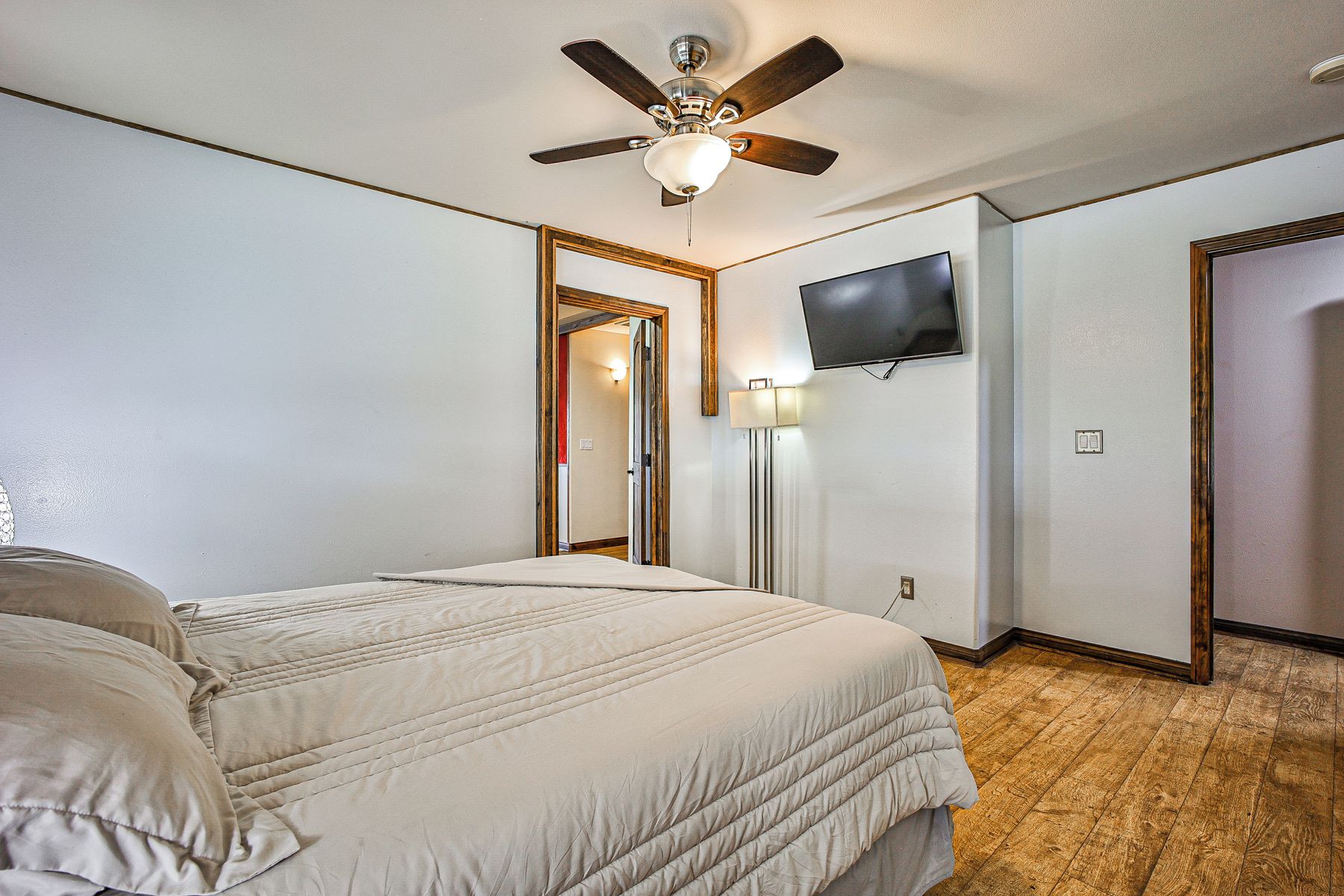 A bedroom with a bed, a ceiling fan, a television, and a door.
