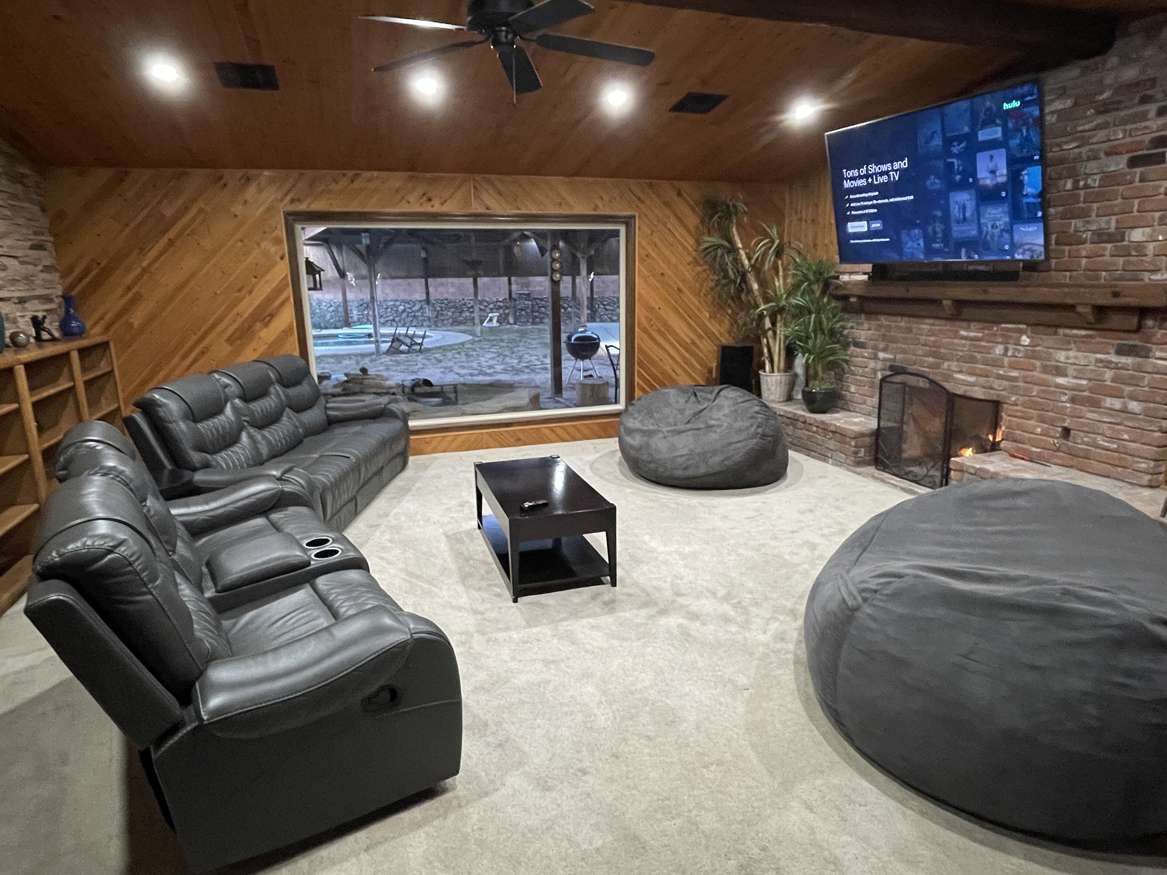 A modern living room with a leather sofa, a round bean bag, a coffee table, and a TV mounted on a brick wall.