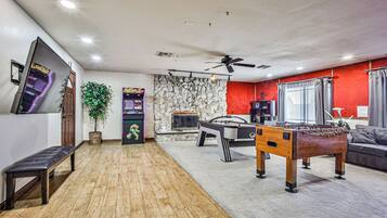 A room with a foosball table, a flat-screen TV, a stone wall, and a ceiling fan.