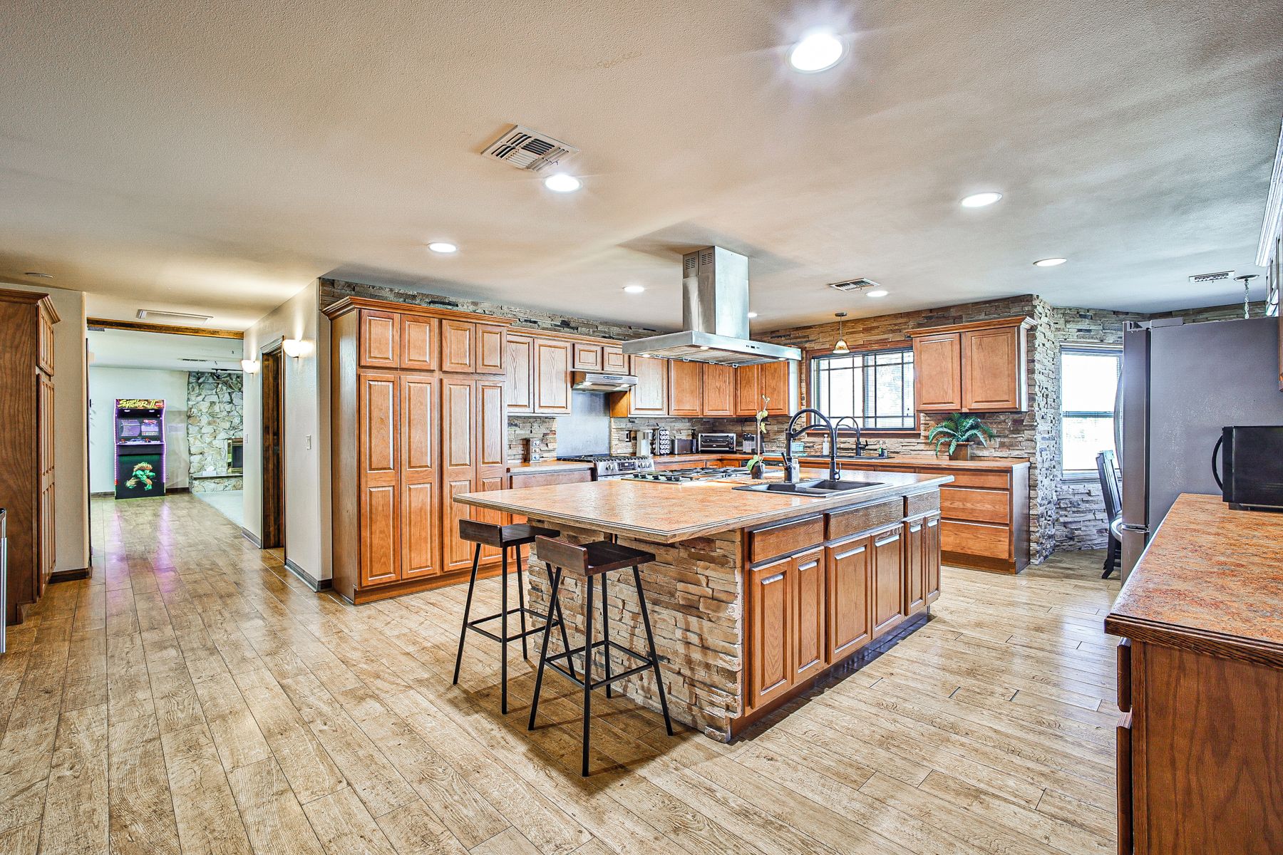 A spacious kitchen with wooden cabinets, a large island with stools, and a stone accent wall.