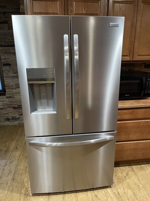Un refrigerador de acero inoxidable con compartimento congelador, dispensador de agua y hielo, e hacedor de hielo incorporado.