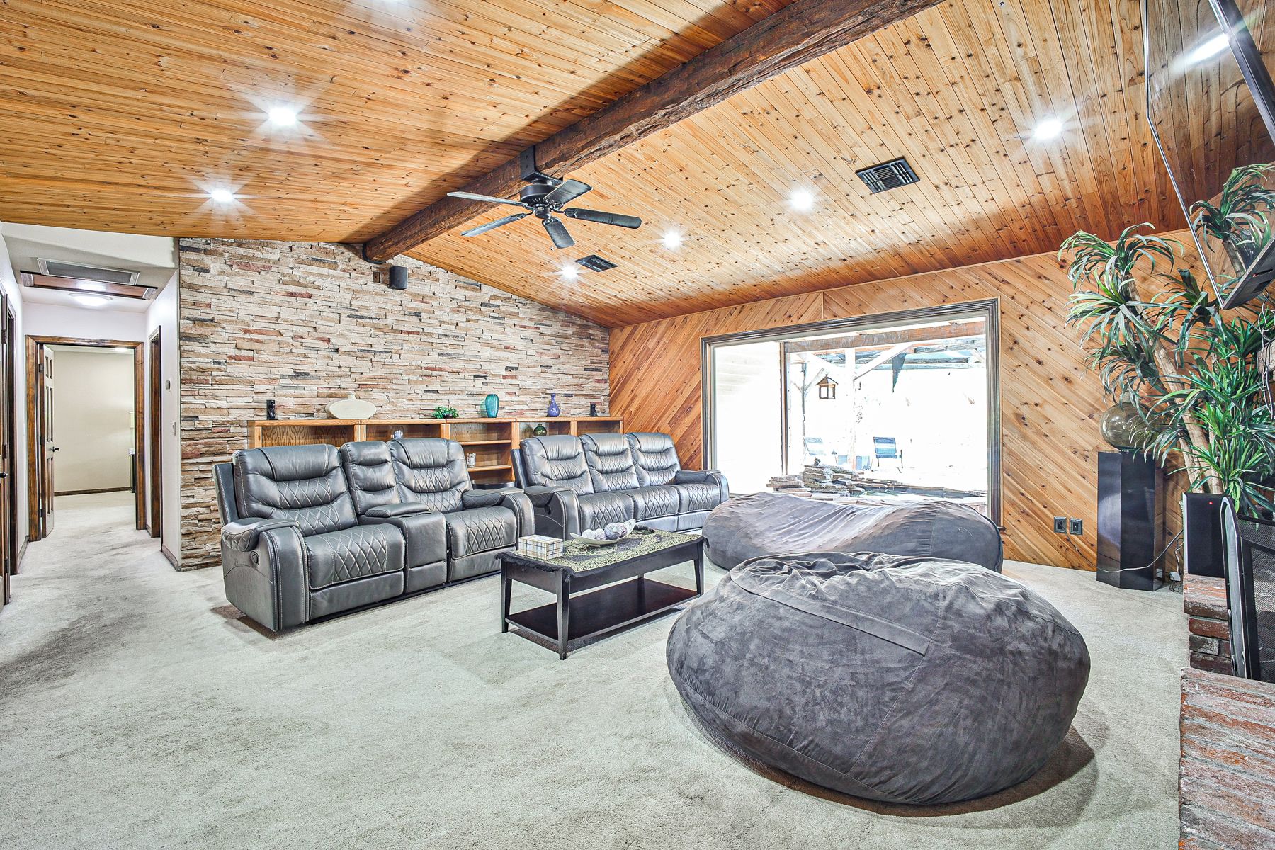 Un salón amplio con pared de piedra, sofás de cuero, un sillón tipo alforza y un ventilador de techo.