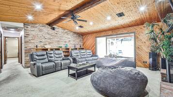 Un salón amplio con pared de piedra, sofás de cuero, un sillón tipo alforza y un ventilador de techo.
