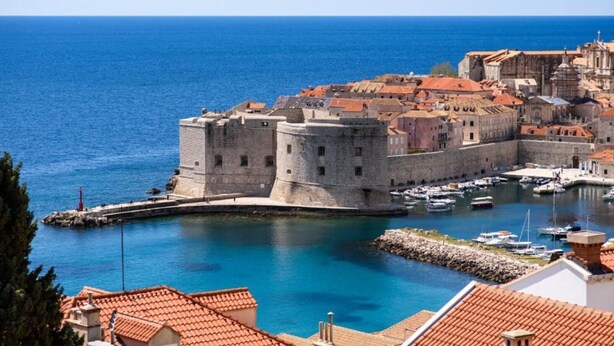 Une ville côtière historique, dotée d’une imposante forteresse en pierre et d’un port de plaisance où sont amarrés des bateaux.