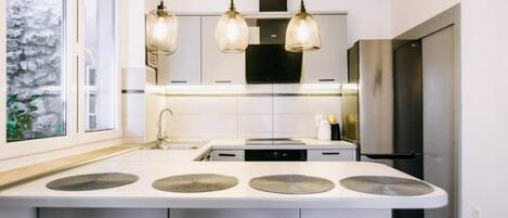 A modern kitchen with a central island, pendant lights, and a view of a stone wall.