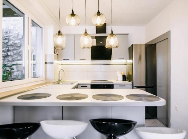 A modern kitchen with a central island, pendant lights, and a view of a stone wall. - One Bedroom Apartment with Terrace (Dubrovnik)