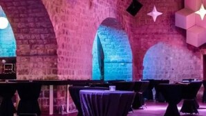 Un intérieur caractérisé par des murs en briques avec des arcs, des tables recouvertes de nappes noires et des luminaires aux formes géométriques.