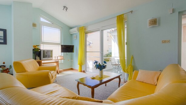 A living room with yellow sofas, a coffee table, a TV, and a balcony with yellow curtains. - Nova- two bedroom apartment with terrace (Zadar)