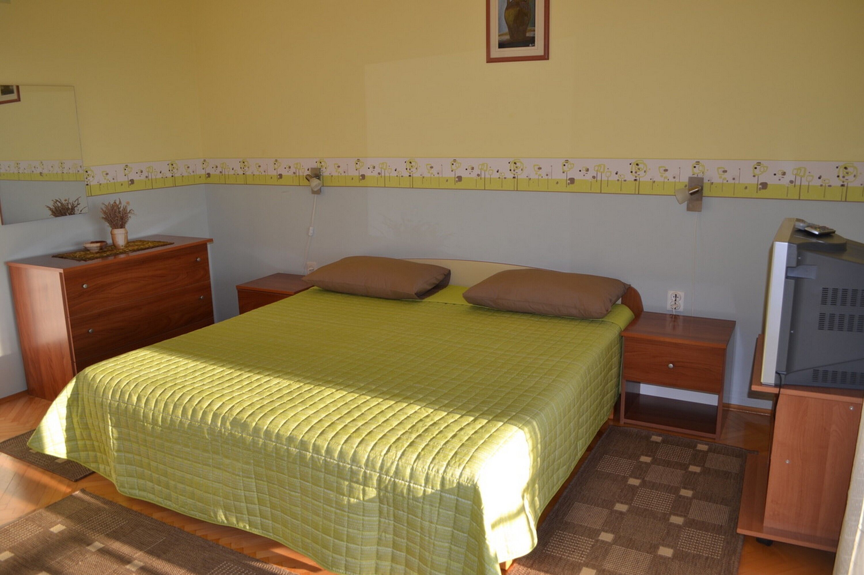 Ein Schlafzimmer mit einem Bett, zwei Nachttischen, einer Kommode, einem Fernseher und einer kleinen Pflanze.