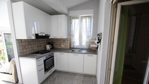 Een kleine keuken met witte kastjes, een gasfornuis, een spoelbak en een raam met gordijnen.
