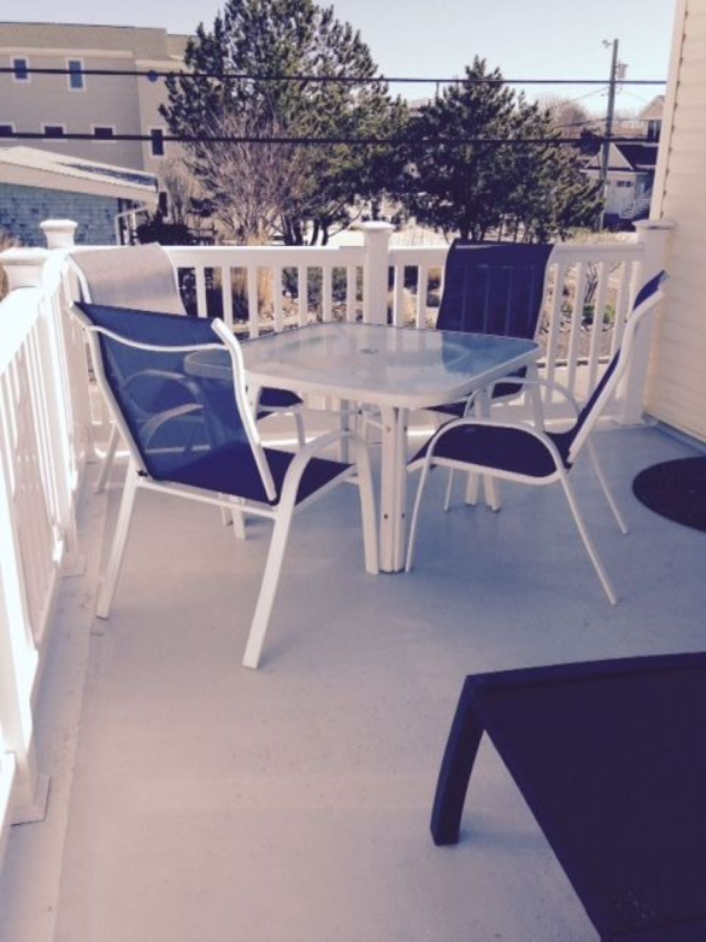 A round table with four chairs on a balcony with a white railing.