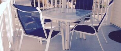 A round table with four chairs on a balcony with a white railing.
