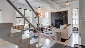 A spacious living area with a fireplace, white sofas, and a staircase leading to another level. - Hôtel à la maison - Le refuge de Louise, avec spa (Weedon)