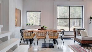 A modern dining area with a wooden table, wicker chairs, and a sofa. - Hôtel à la maison - Le refuge de Louise, avec spa (Weedon)
