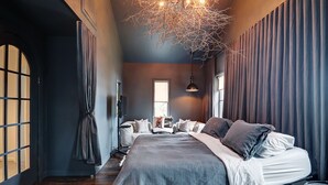 A modern bedroom with a large bed, a hanging light fixture, and a view of the outdoors through a window. - Hôtel à la maison - Le refuge de Louise, avec spa (Weedon)