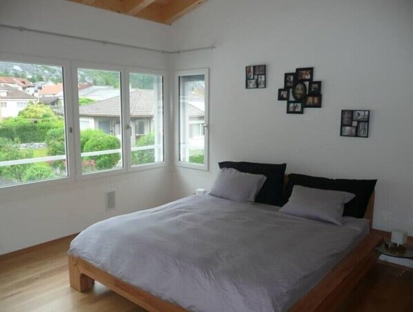 A bedroom with a large window, a bed with a wooden frame, and several framed pictures on the wall. - Brand New Open Concept Whole House (Felsberg)