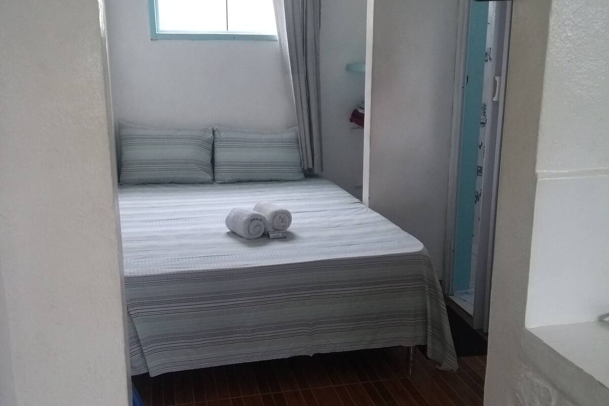 Ein kleiner, schmaler Raum mit einem Einzelbett, einem Fenster mit Vorhängen und Holzboden.