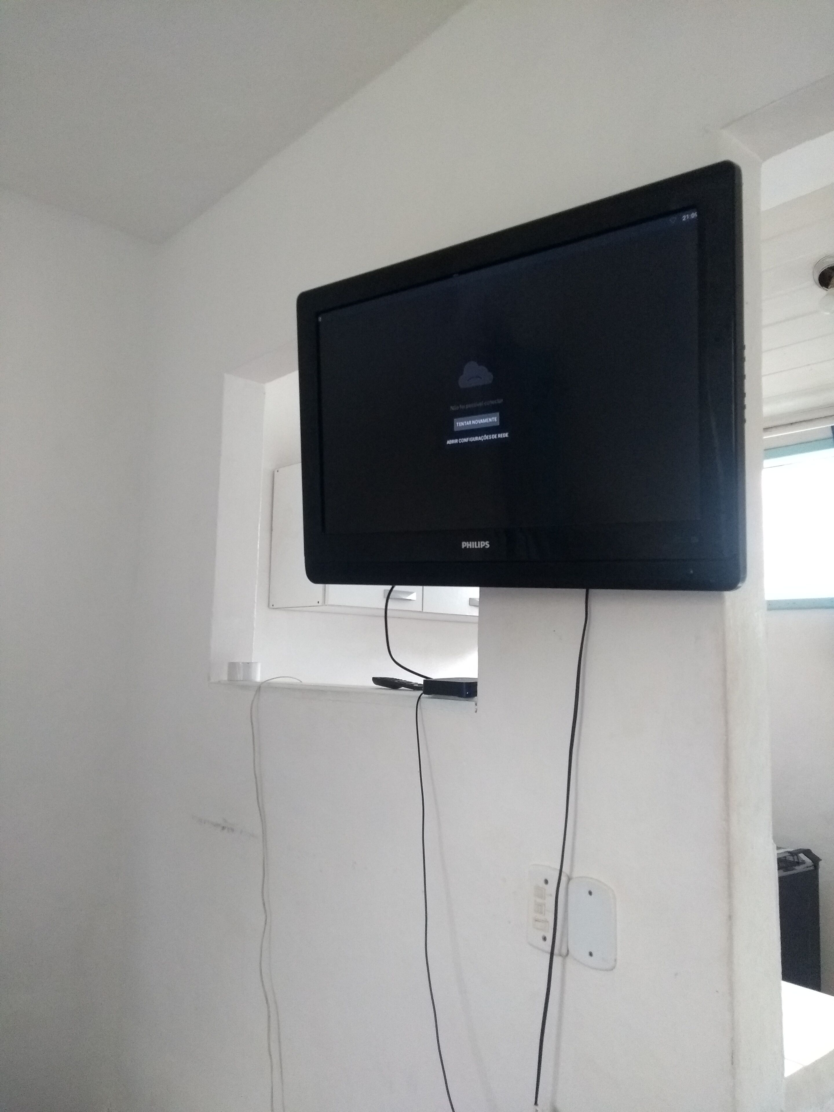 Un téléviseur Philips noir fixé sur un mur blanc, avec deux câbles apparents qui y sont connectés.