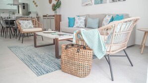 Un salon moderne avec un canapé, des fauteuils en osier, une table à manger et une cuisine en arrière-plan.