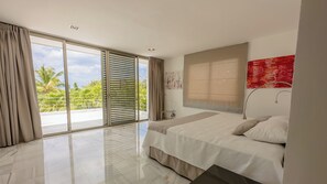 Une chambre moderne dotée d’une grande porte-fenêtre coulissante donnant sur un balcon, d’un lit avec une tête de lit et d’un tableau abstrait rouge accroché au mur.