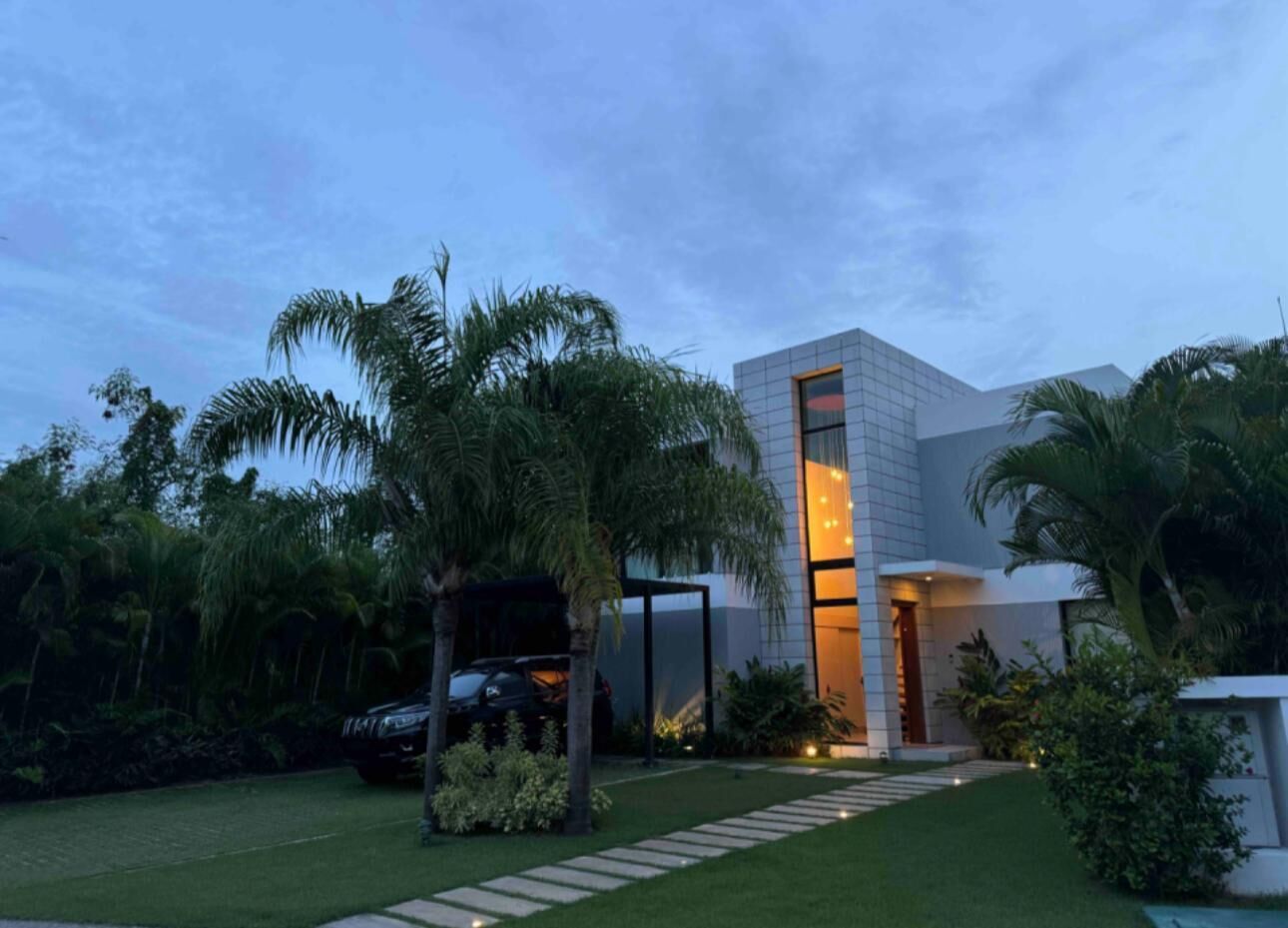 A modern house with a large glass door, surrounded by a well-maintained garden and palm trees.