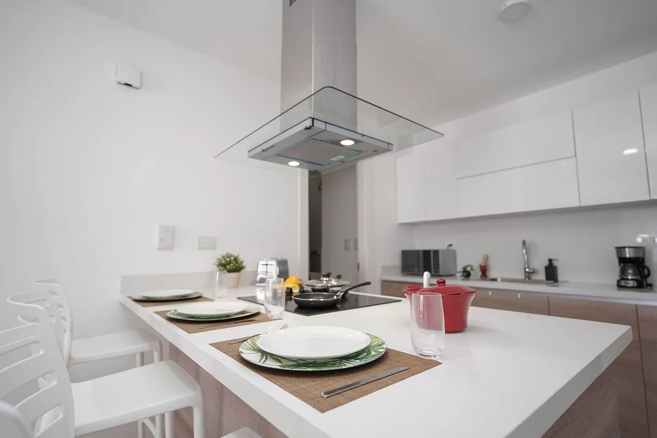 A modern kitchen with a central island, white cabinetry, and a glass hood over the stove.
