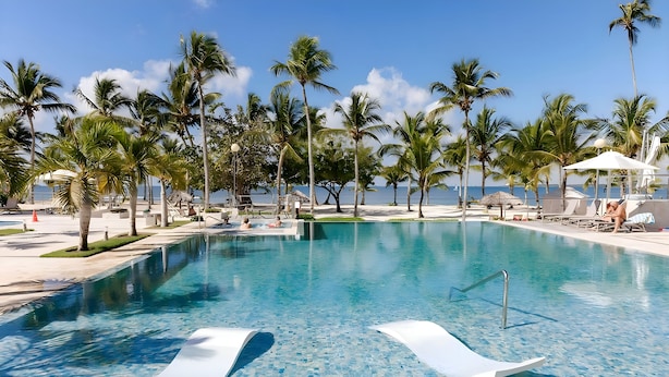 Une piscine d’un bleu éclatant, entourée de palmiers et de chaises longues, avec vue sur l’océan.