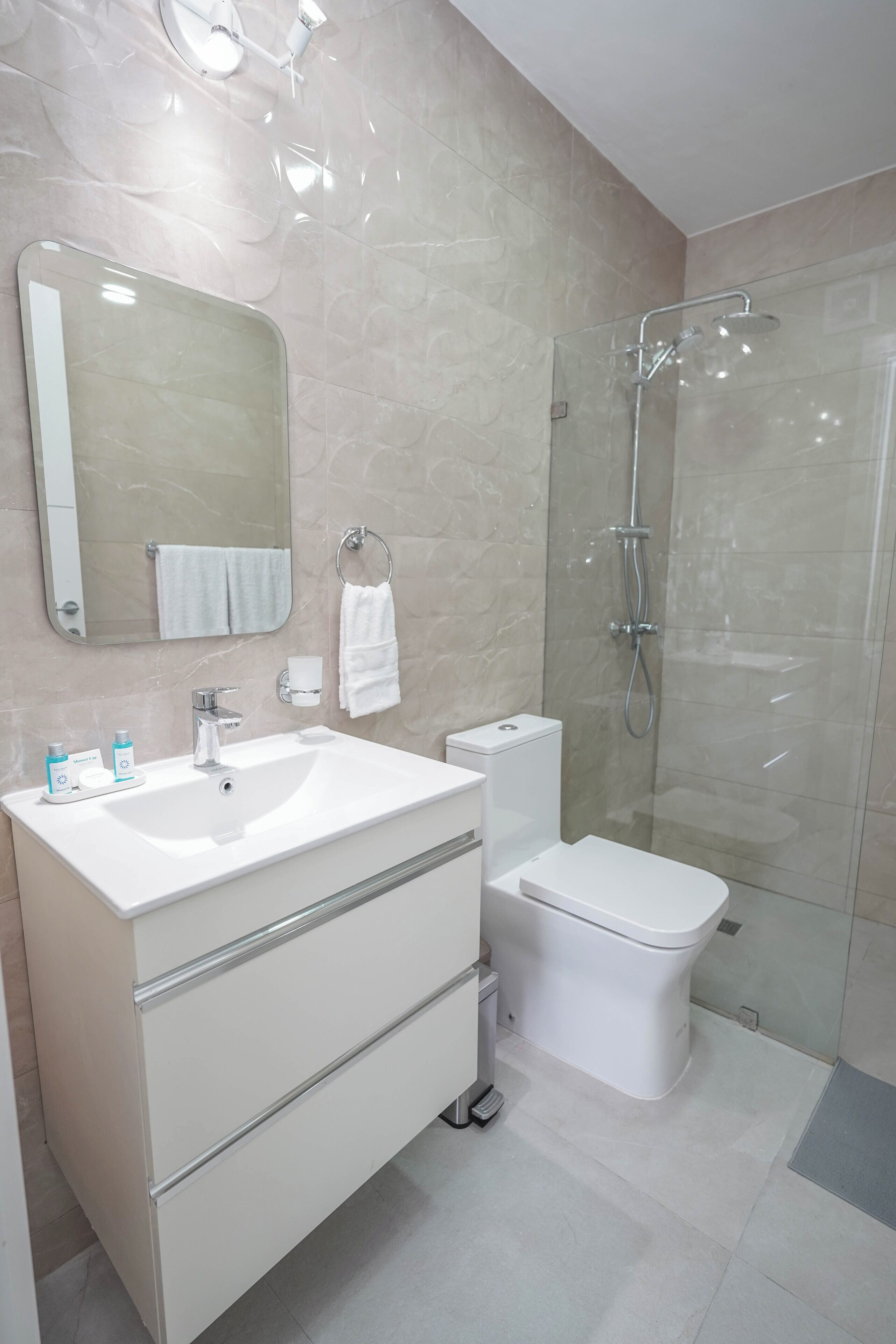 Un baño moderno con un espejo grande, un lavamanos blanco, un inodoro y una ducha con cerramiento de vidrio.